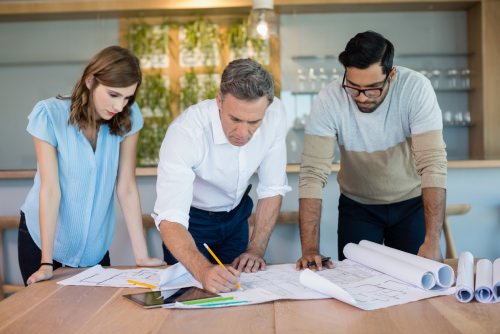 Three people standing over a desk looking at blueprints
