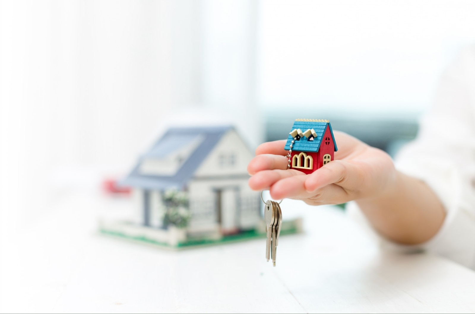 A hand holding a set of keys with a tiny house keychain